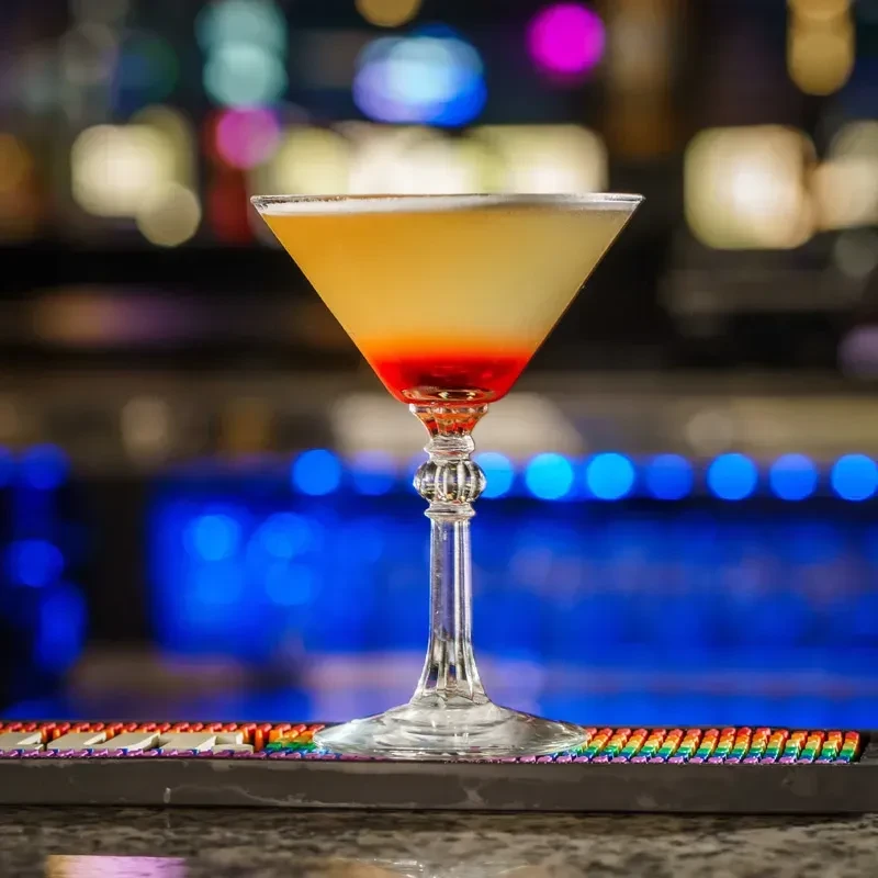 Layered yellow and red cocktail in martini glass on rainbow mat.