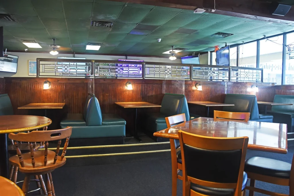 Dining area of a pub with wooden tables, teal booths, stained glass partition.