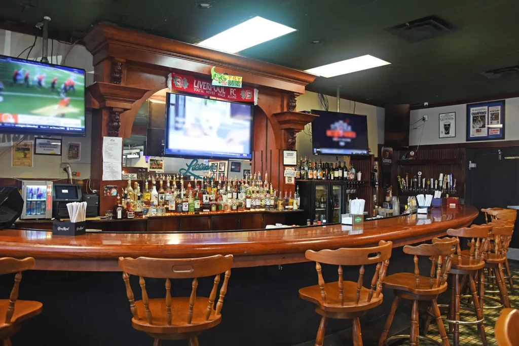 Classic wooden bar with stools, liquor, draft taps, and sports TVs.
