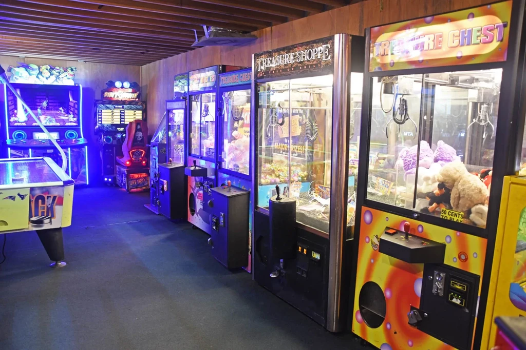 Empty arcade with air hockey, prize claw machines, and neon-lit video games.
