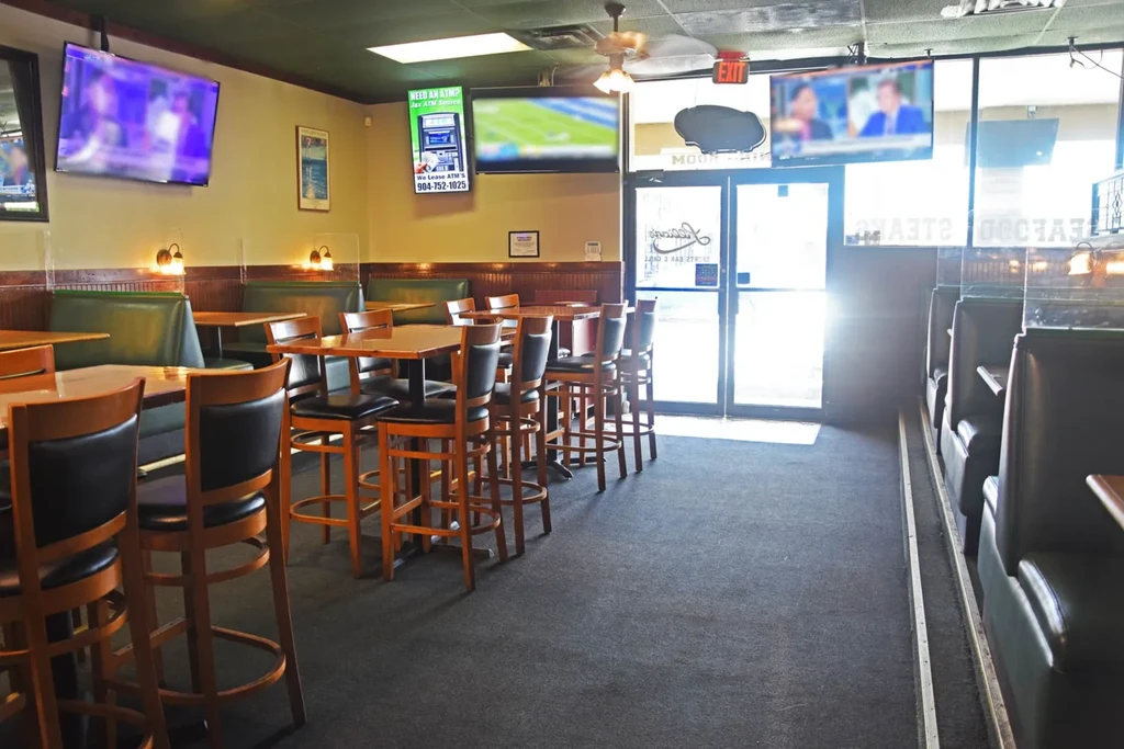 A brightly lit, empty casual restaurant with green booths and TVs.