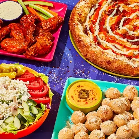Colorful spread of wings, pizza, salad, and fried dough on a purple table.