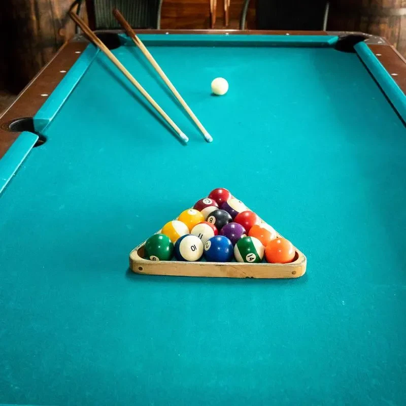 Teal pool table with a triangle of billiard balls and two cues.