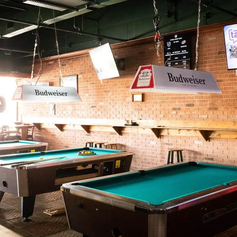 Multiple pool tables in an empty bar with brick walls and industrial lights.