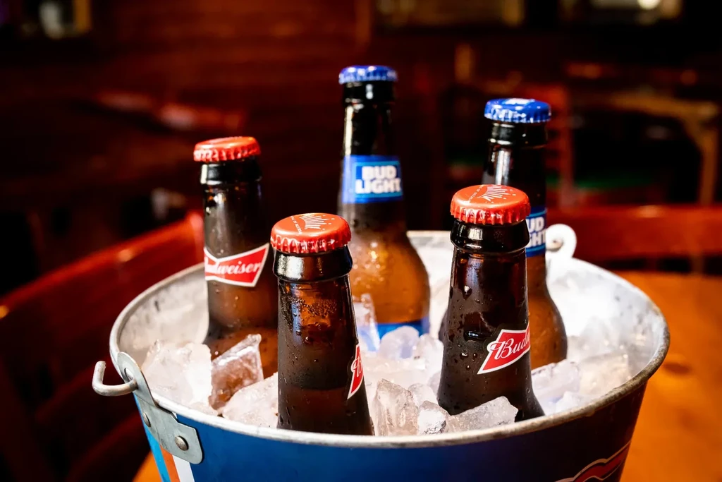 Cold Budweiser and Bud Light bottles in a blue striped ice bucket.