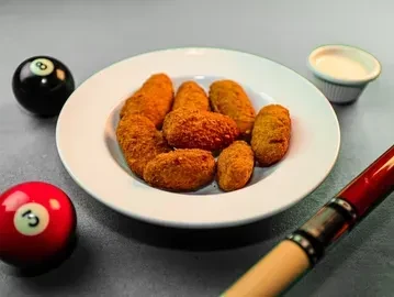 Breaded snacks, dipping sauce, and billiard balls on a pool table.
