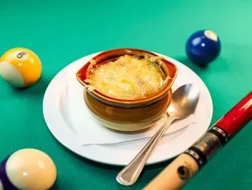 Cheesy gratin in a rustic bowl on a pool table with billiard balls.