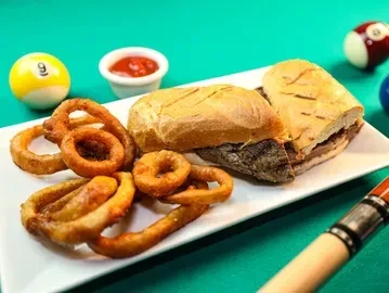 Onion rings, sandwich, and ketchup on a plate on a billiard table.