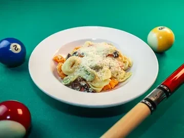Cheesy tortellini pasta on a green pool table with billiard balls.