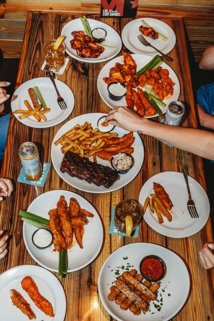 Overhead of people sharing a table of bar food and cocktails.