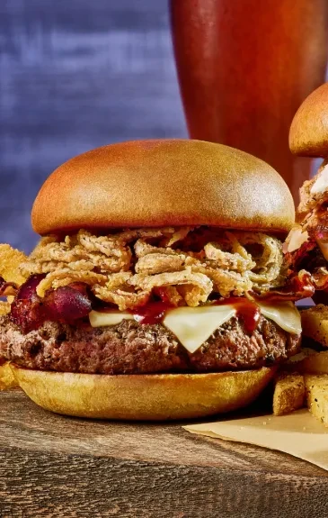 Detailed burger with beef, cheese, bacon, onion strings, sauce, fries, and beer.