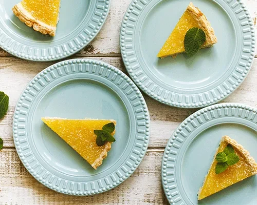 Four vibrant lemon tart slices with mint on blue plates.