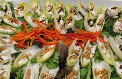 Platter of endive appetizers with creamy filling, figs, and colorful vegetable garnish.