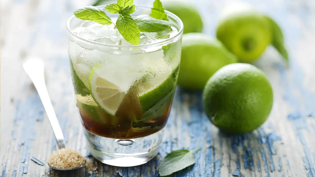 Iced mojito-like drink with lime, mint, brown sugar, and limes on wood.