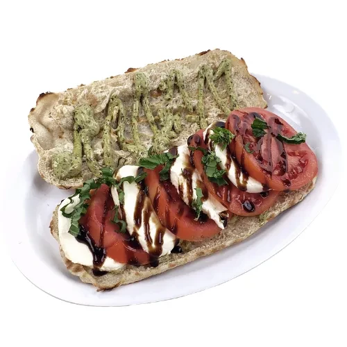 Open baguette halves with tomatoes, mozzarella, basil, pesto, balsamic glaze.