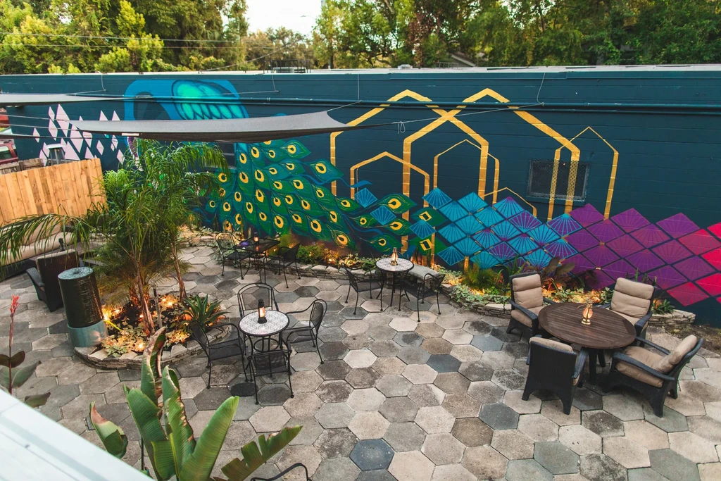Outdoor patio with vibrant peacock mural, diverse seating, and lush plants.