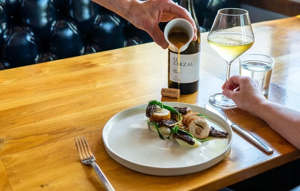 Server pours sauce on rolled meat dish with white wine.