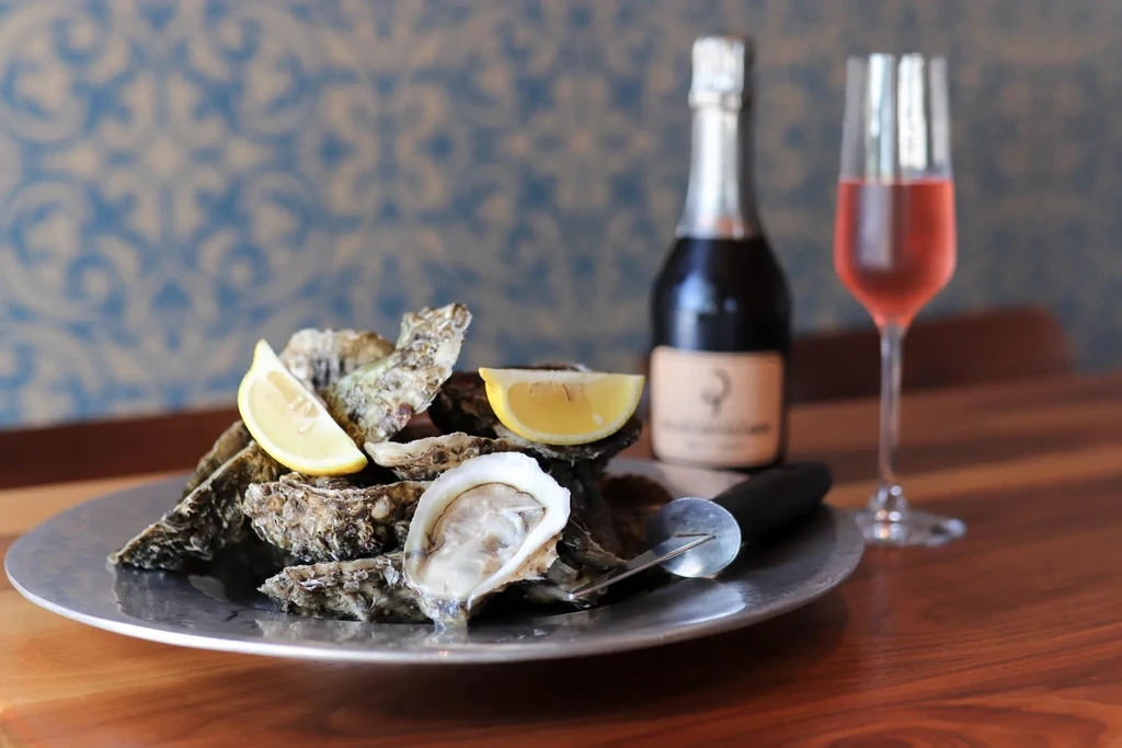 Glistening oysters with lemon wedges, shucking knife, sparkling wine, and rosé.