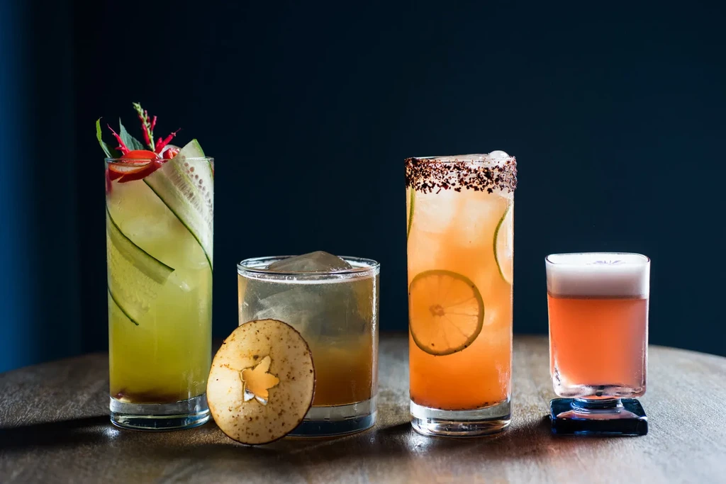 Four colorful, artfully garnished cocktails on a dark wooden table.