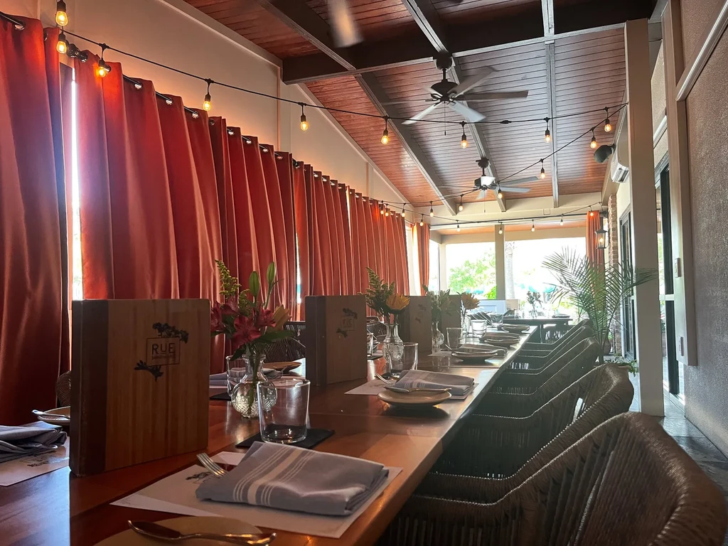 Restaurant interior: long set table, string lights, and lush tropical patio.