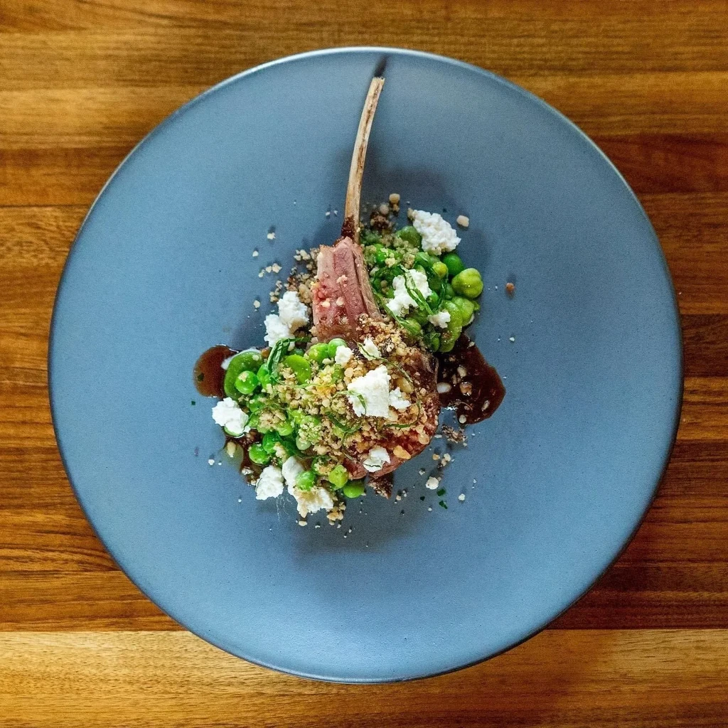 Overhead: plated lamb chop, vibrant green peas, crumbled white cheese.