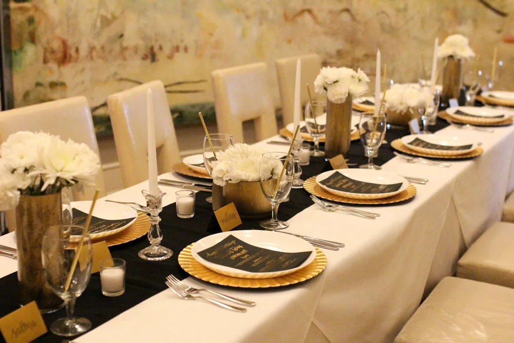 Formal dining table set with gold chargers, white flowers, candles, and menus.