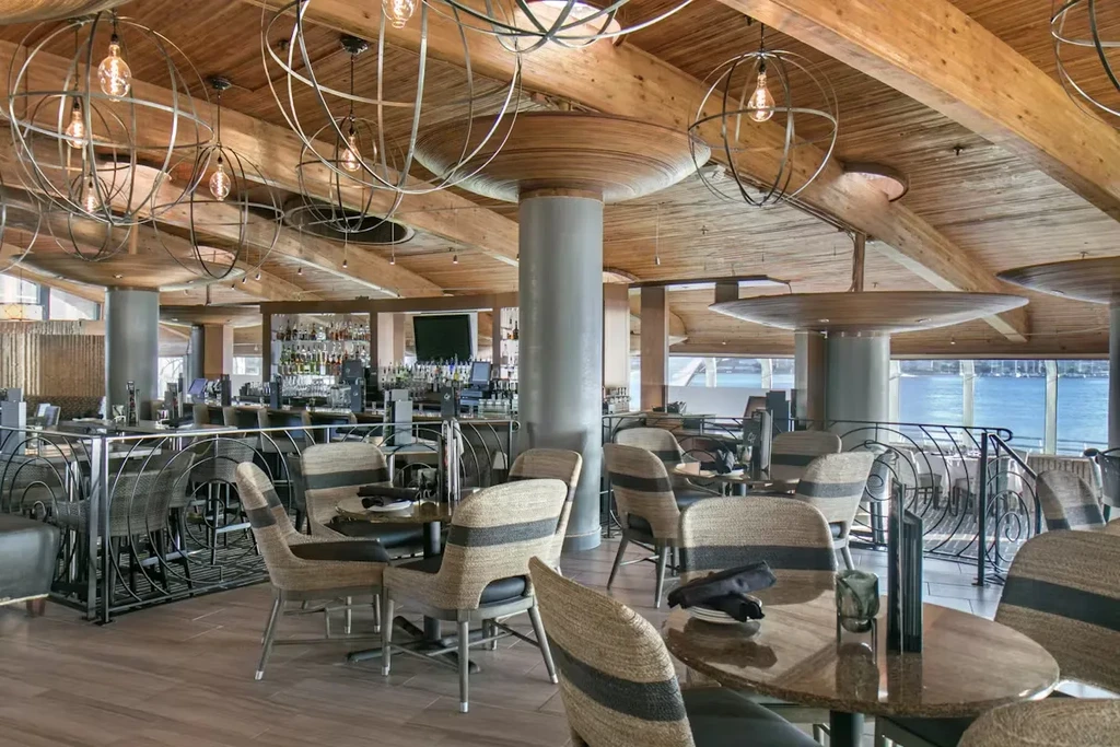 Modern restaurant with wooden beams, extensive bar, and waterfront view.
