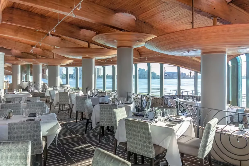 Elegant restaurant with sculptural wood ceiling and panoramic city waterfront view.