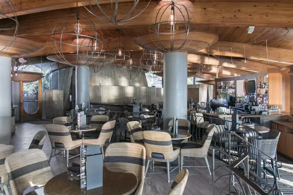 Empty modern restaurant with unique chairs, wooden ceiling, and stocked bar.