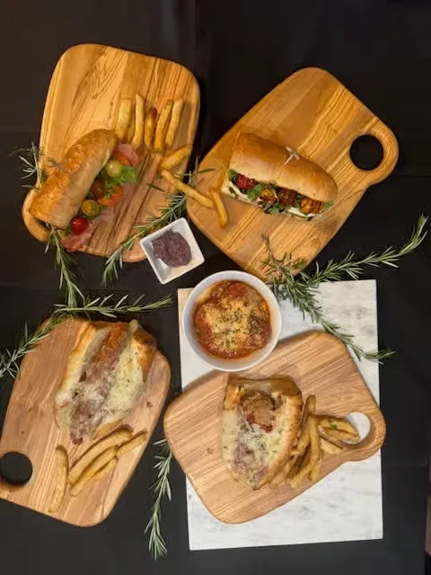 Multiple subs, fries, and a cheesy dish on wooden boards, overhead.