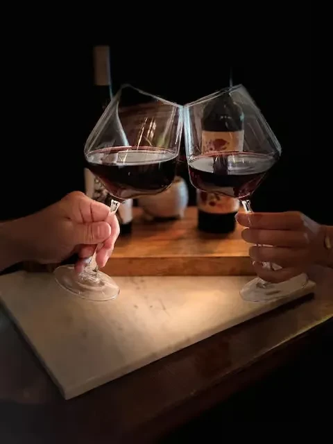 Two hands clink elegant angular red wine glasses in a toast.