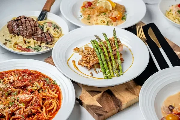 Overhead, several gourmet pasta and protein dishes in an elegant setting.
