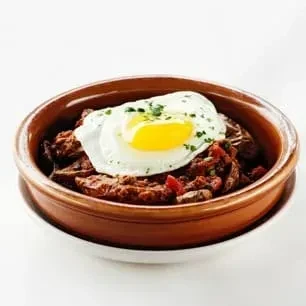 Hearty stew in rustic bowl topped with sunny-side-up egg and herbs.