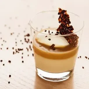 Layered cream and caramel dessert in glass, with brittle and sprinkles.