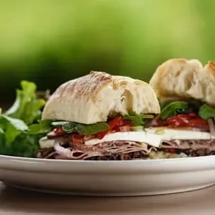 Two halves of an artisan sandwich with meat, cheese, and vegetables.