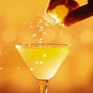 Cocktail in martini glass with hand squeezing lemon over it.