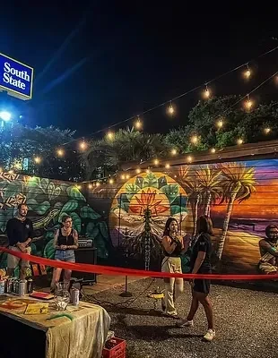 Lively night gathering under string lights, with murals and people.