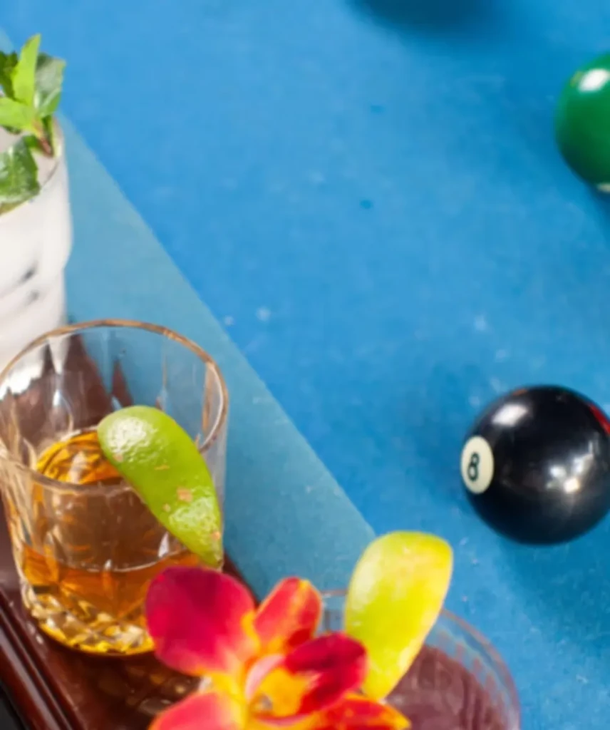 Close-up of two drinks, orchid, and 8-ball on blue pool table.