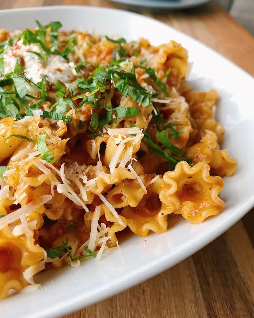 Star-shaped pasta with reddish sauce, grated cheese, herbs, and ricotta.