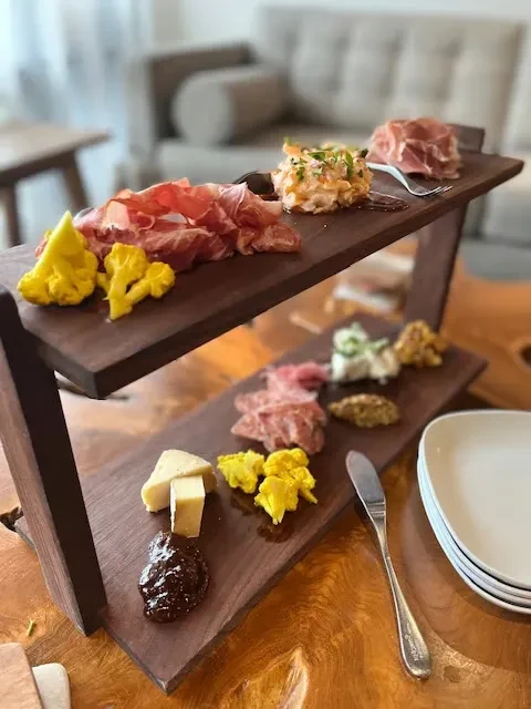 Rustic two-tier board with meats, cheeses, pickled cauliflower, and jam.
