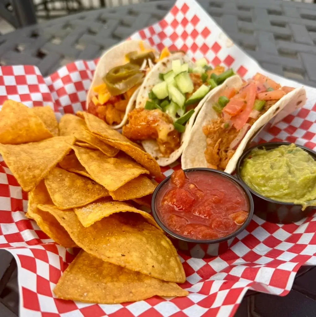 Three tacos, chips, salsa, and guacamole in a checkered basket.