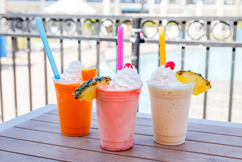Three colorful frozen drinks with whipped cream and fruit on an outdoor table.
