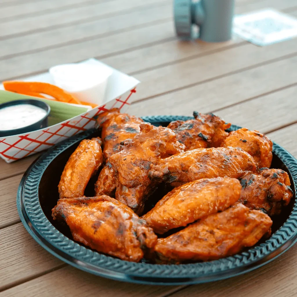 Glossy buffalo wings with celery, carrots, and dipping sauce on wood.