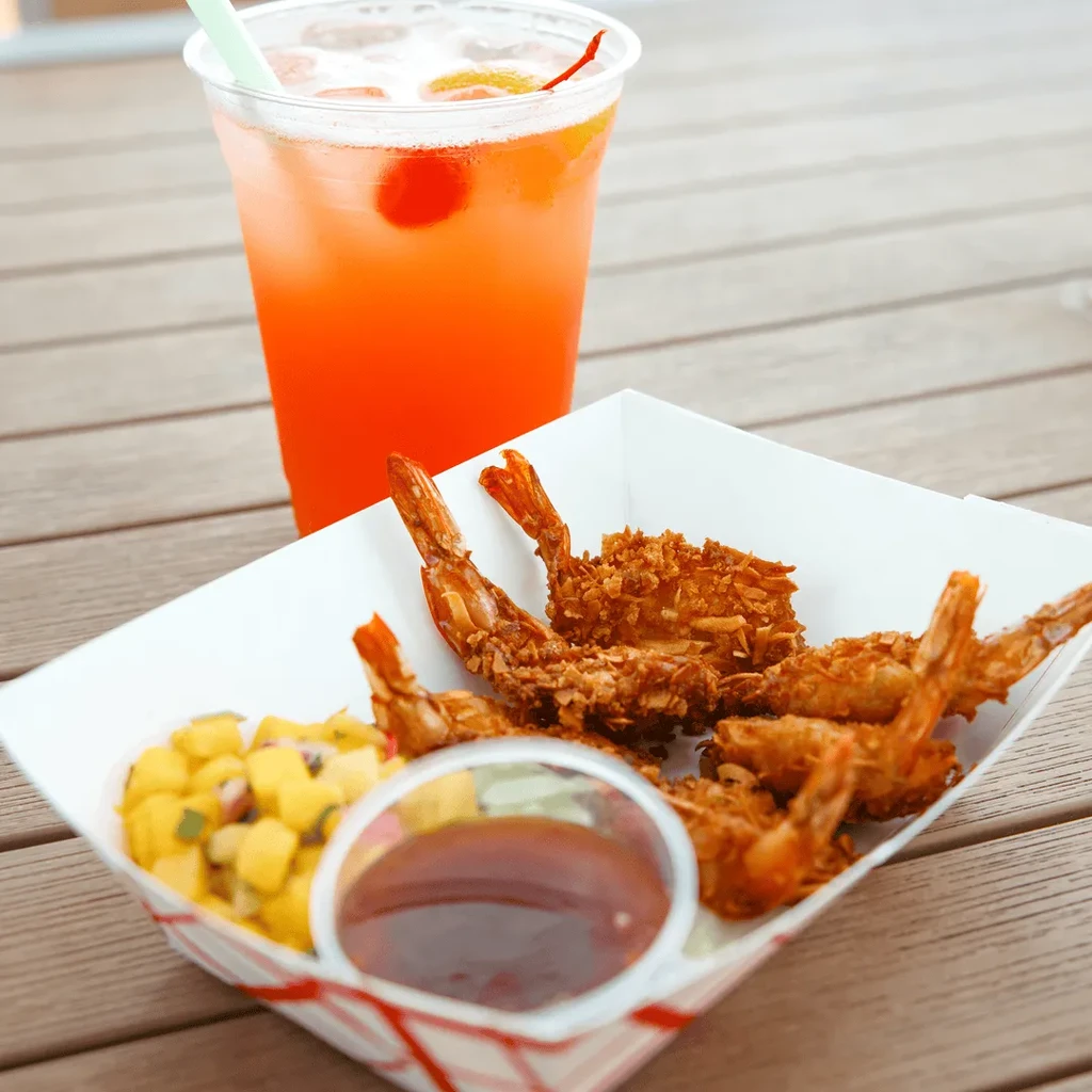 Fried shrimp, mango salsa, and a cocktail on an outdoor wooden table.