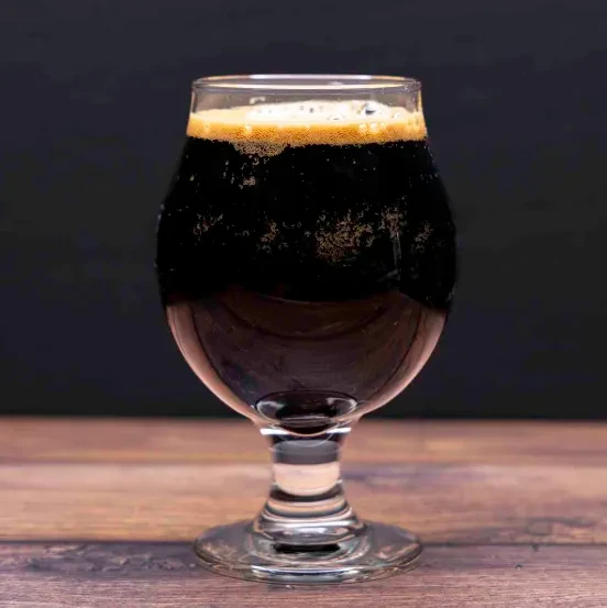 Stemmed glass of dark beer with creamy tan head on rustic wood.