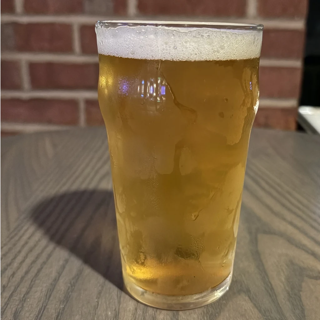 A cold glass of frothy amber beer on a wooden table.