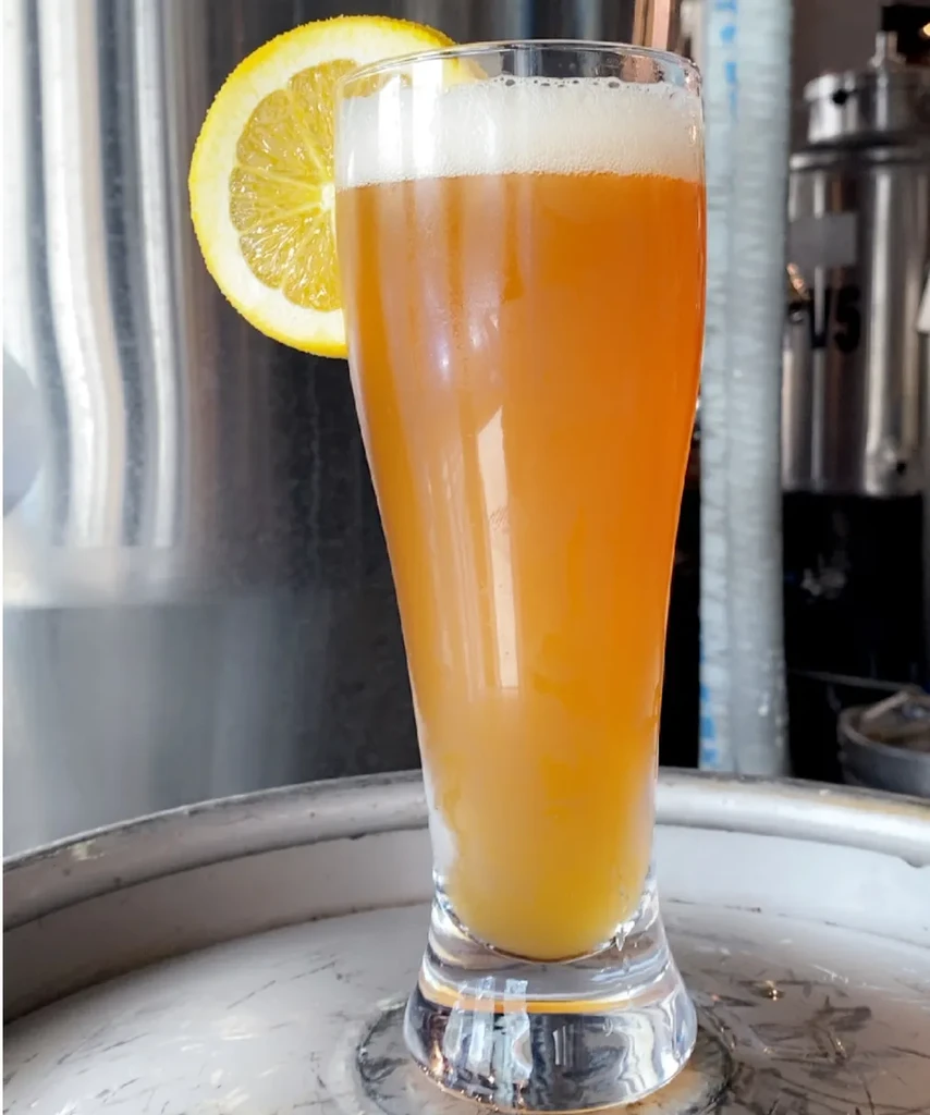 Amber drink in glass with foam and citrus, brewery background.