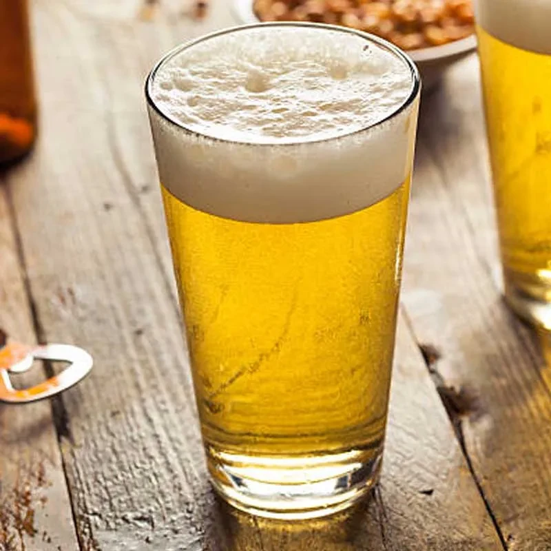 A pint of golden beer with foam, on a rustic table.