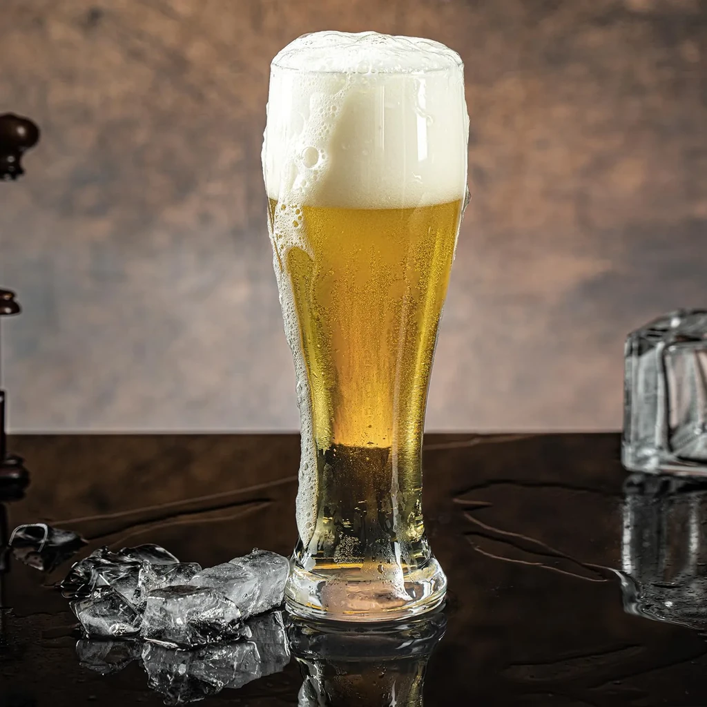 Pilsner glass of golden beer, frothy head, condensation, ice on reflective surface.