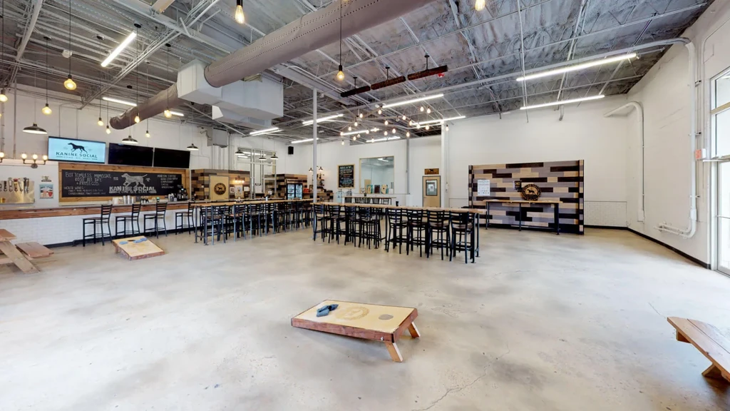 Industrial-style Kanine Social bar interior with high-top tables and cornhole.